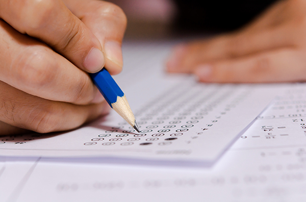 Student's hand holding pencil and filling in selected choice on answer sheet for math test.